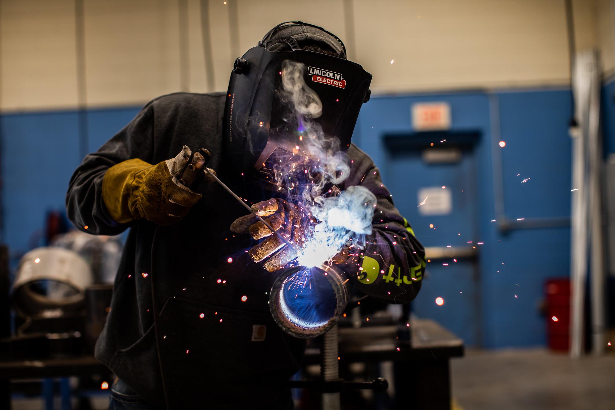 student stick welds a pipe with a mask on