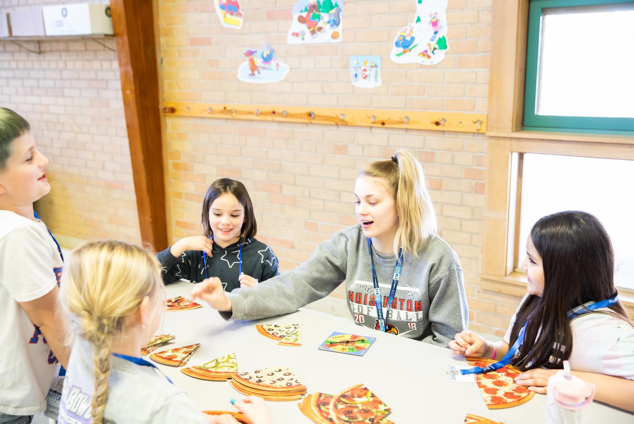 college student playing a game with cardboard pizza pieces with grade school students