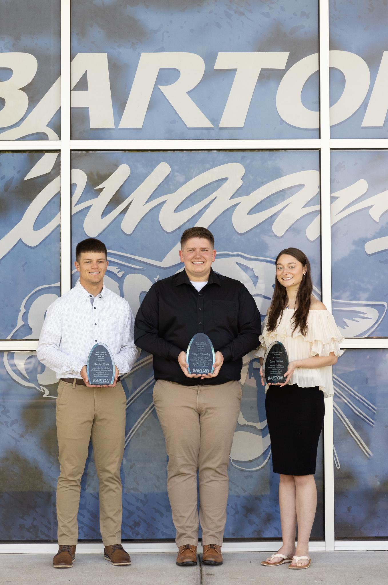 3 people holding awards in front of a blue backdrop