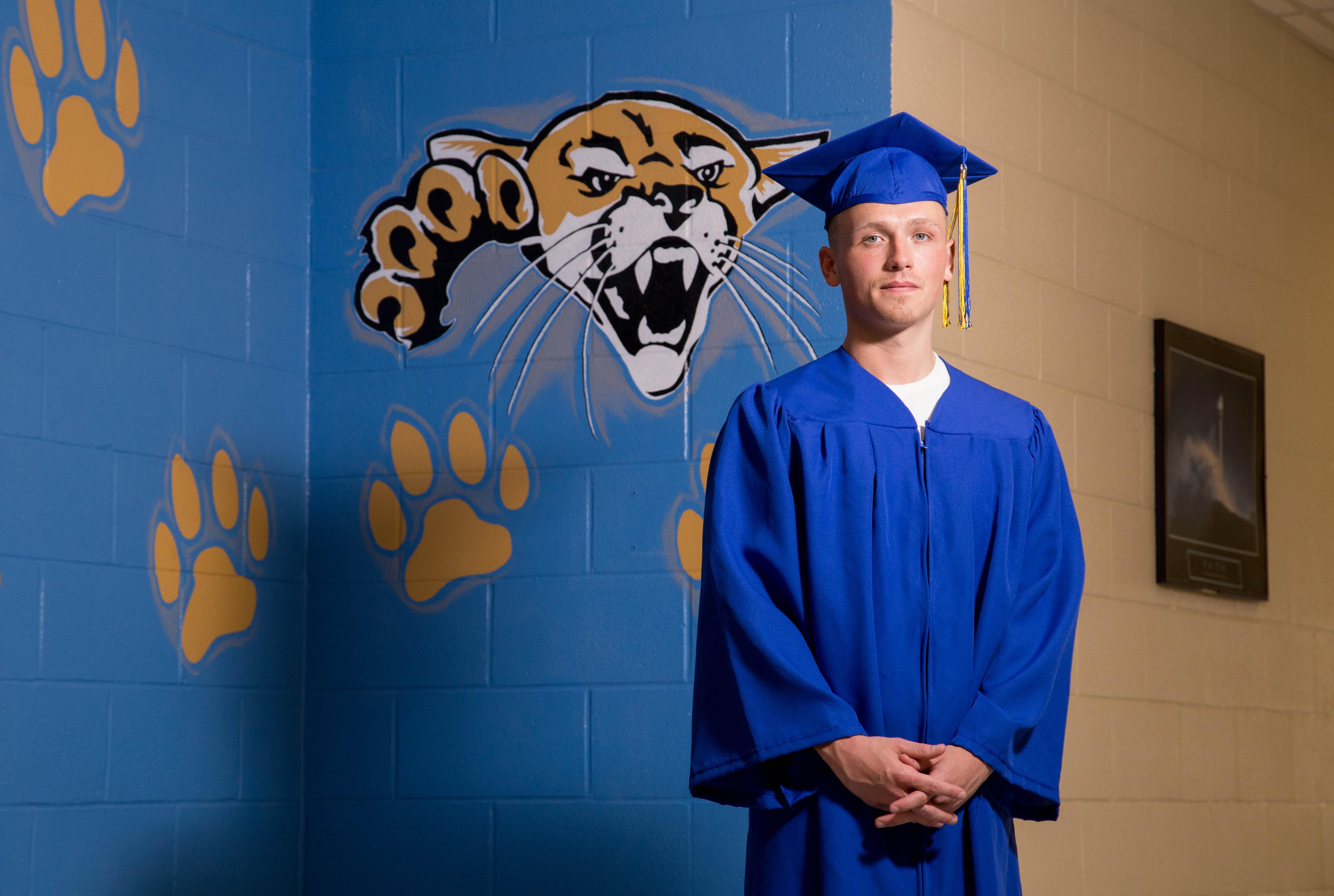 graduate in cap and gown in front of cougar on wall