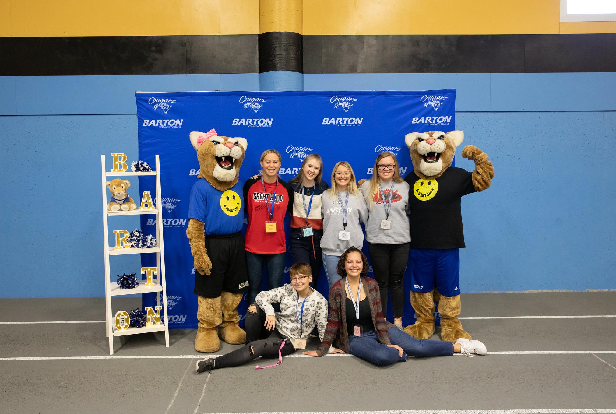 group of students standing with mascots in front of a branded backdrop
