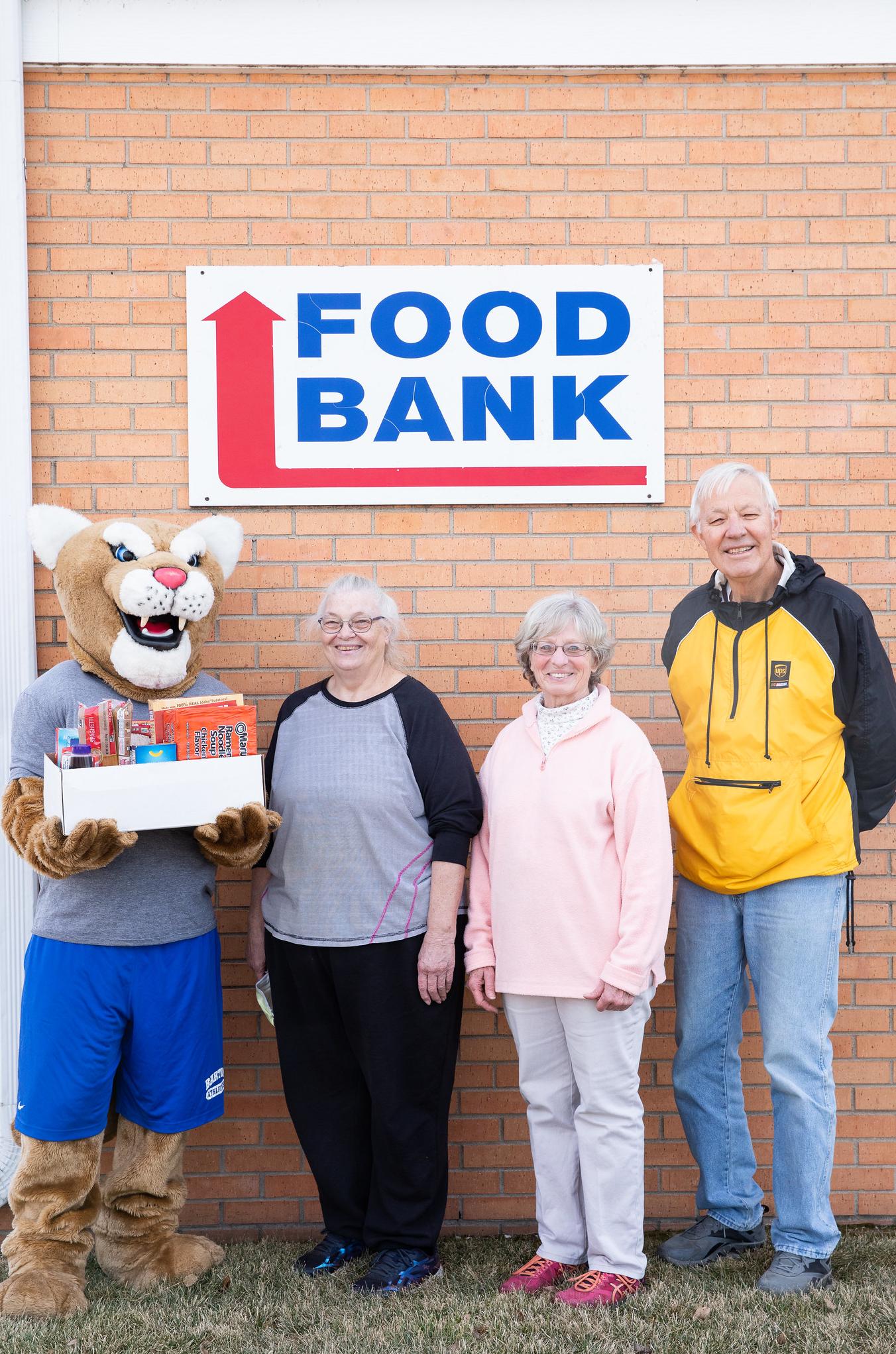 bart the cougar mascot holding food with food bank representatives next to him under the food bank sign