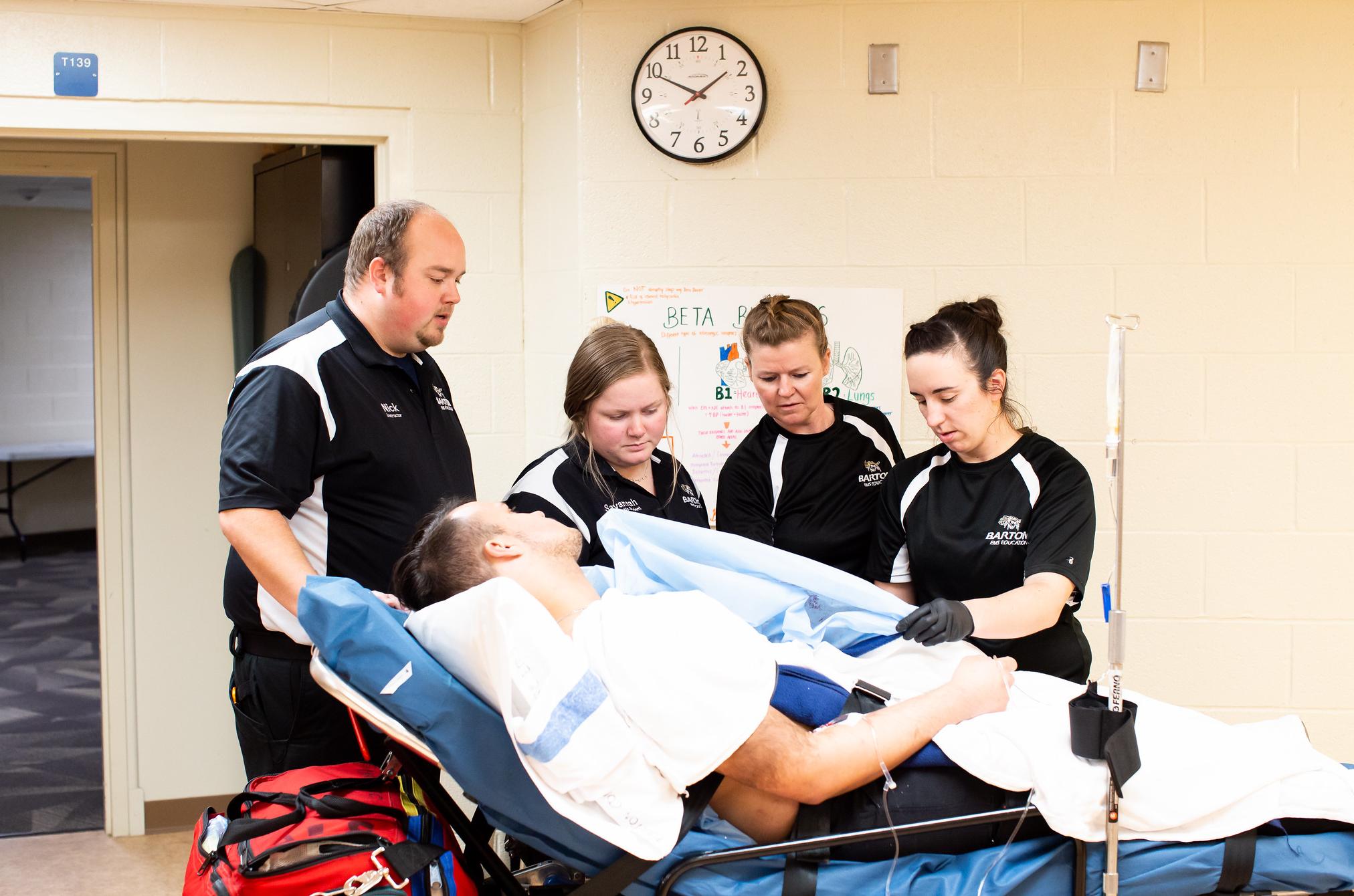 Students and instructor running a paramedic or emt drill with a live patient