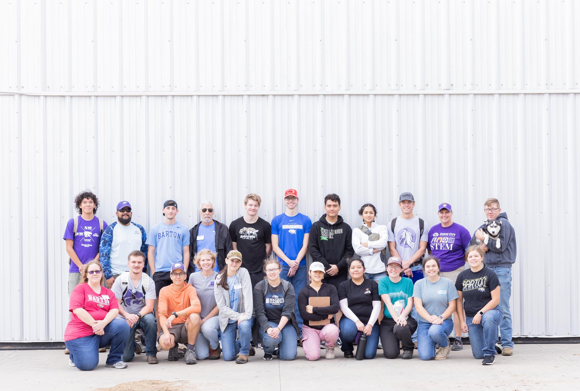 large group of students in front of a metal building in hats, jeans, boots