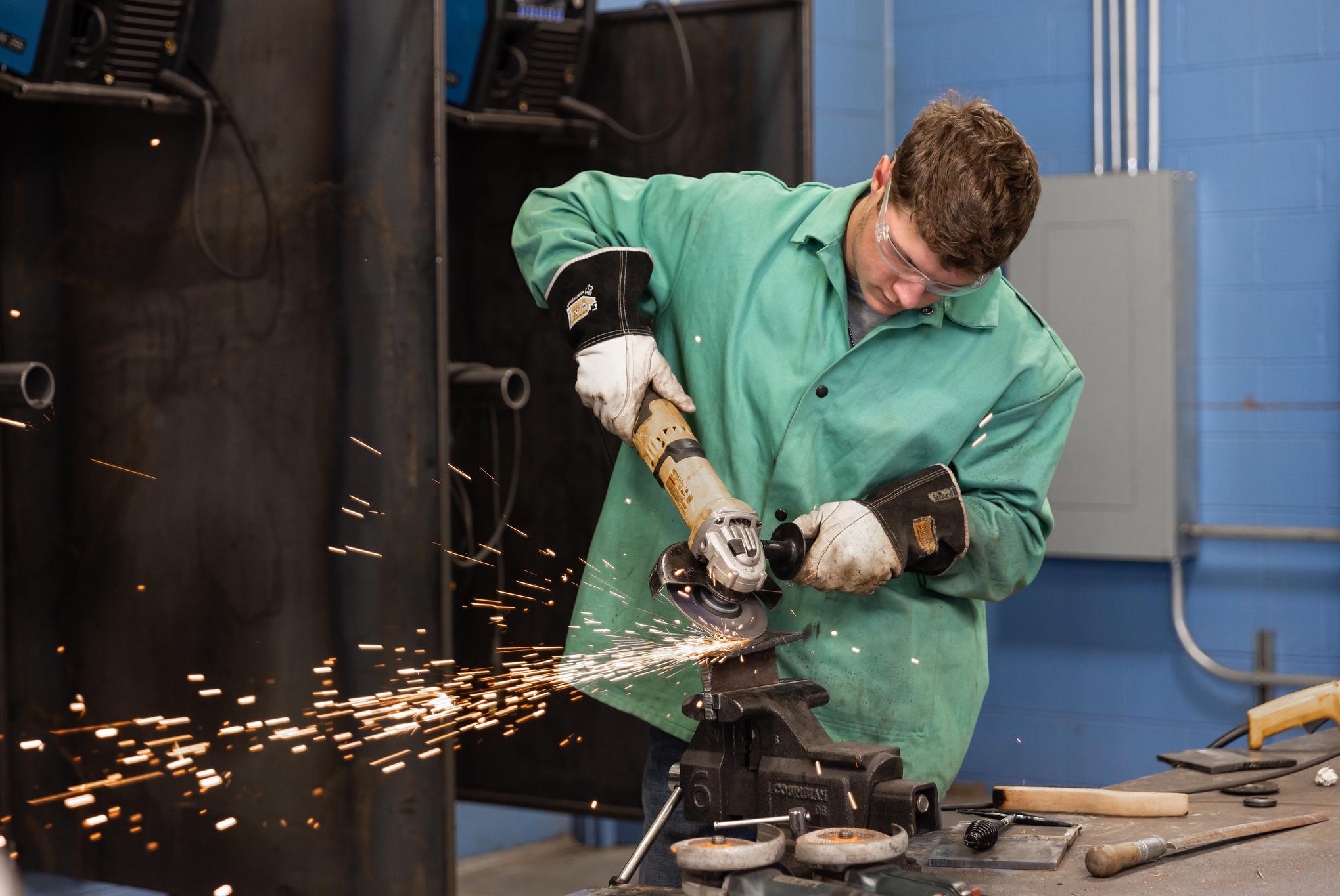 male student uses a grinder on a piece of metal creating a shower of sparks