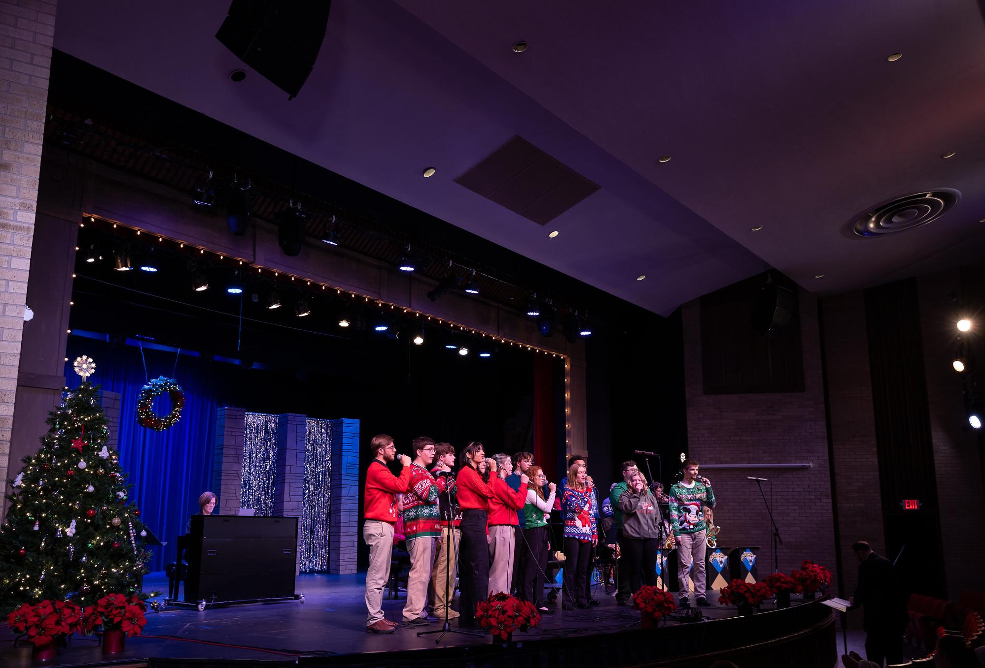 singers singing in holiday sweaters and christmas trees on the stage