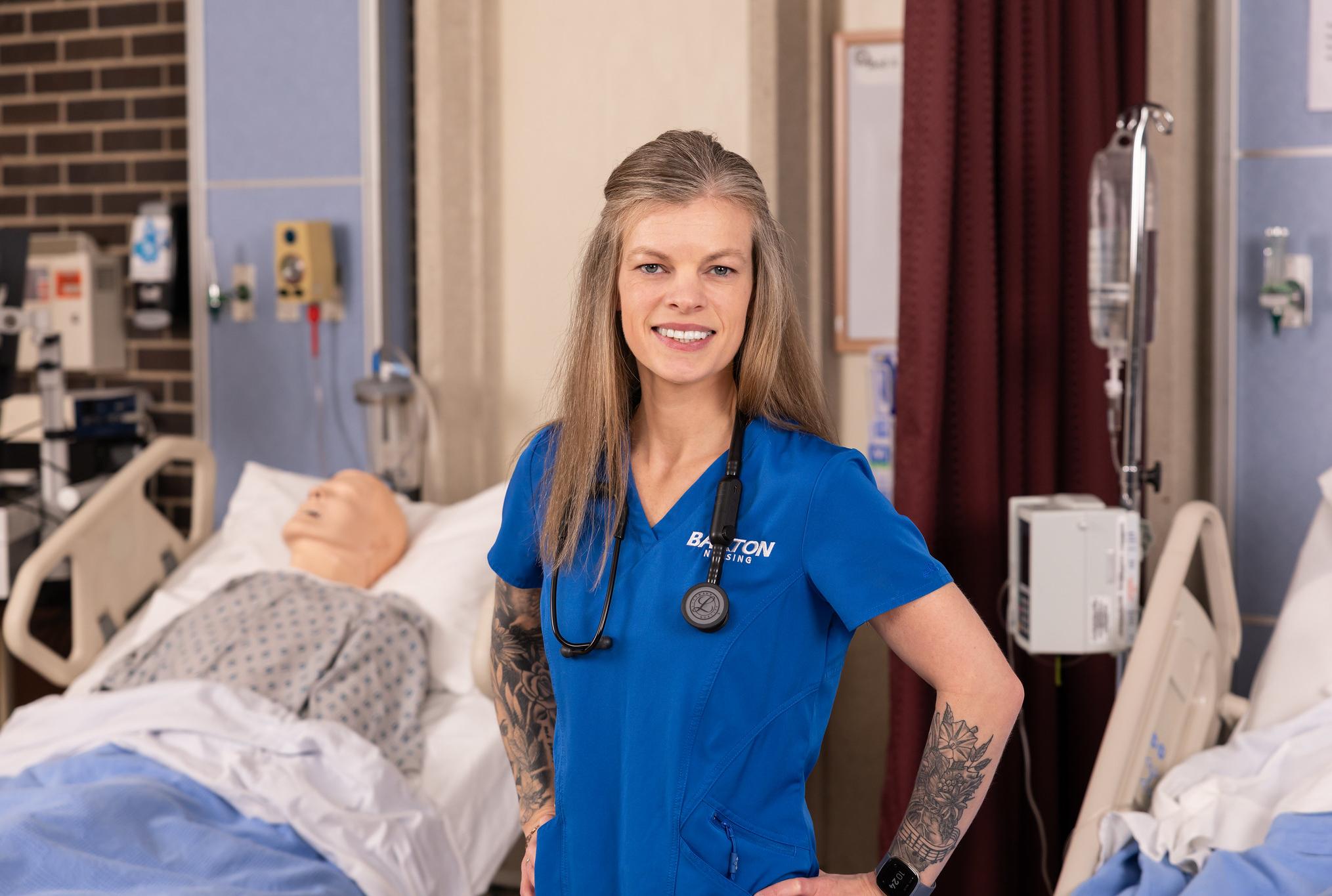 Nurse with hands on hips with mannequin on hospital bed in background