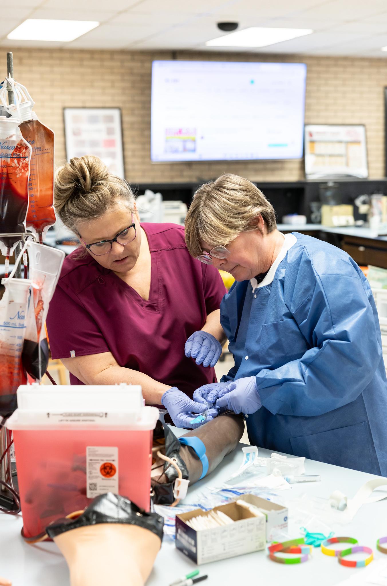 teacher helping a student put a needle in a fake arm