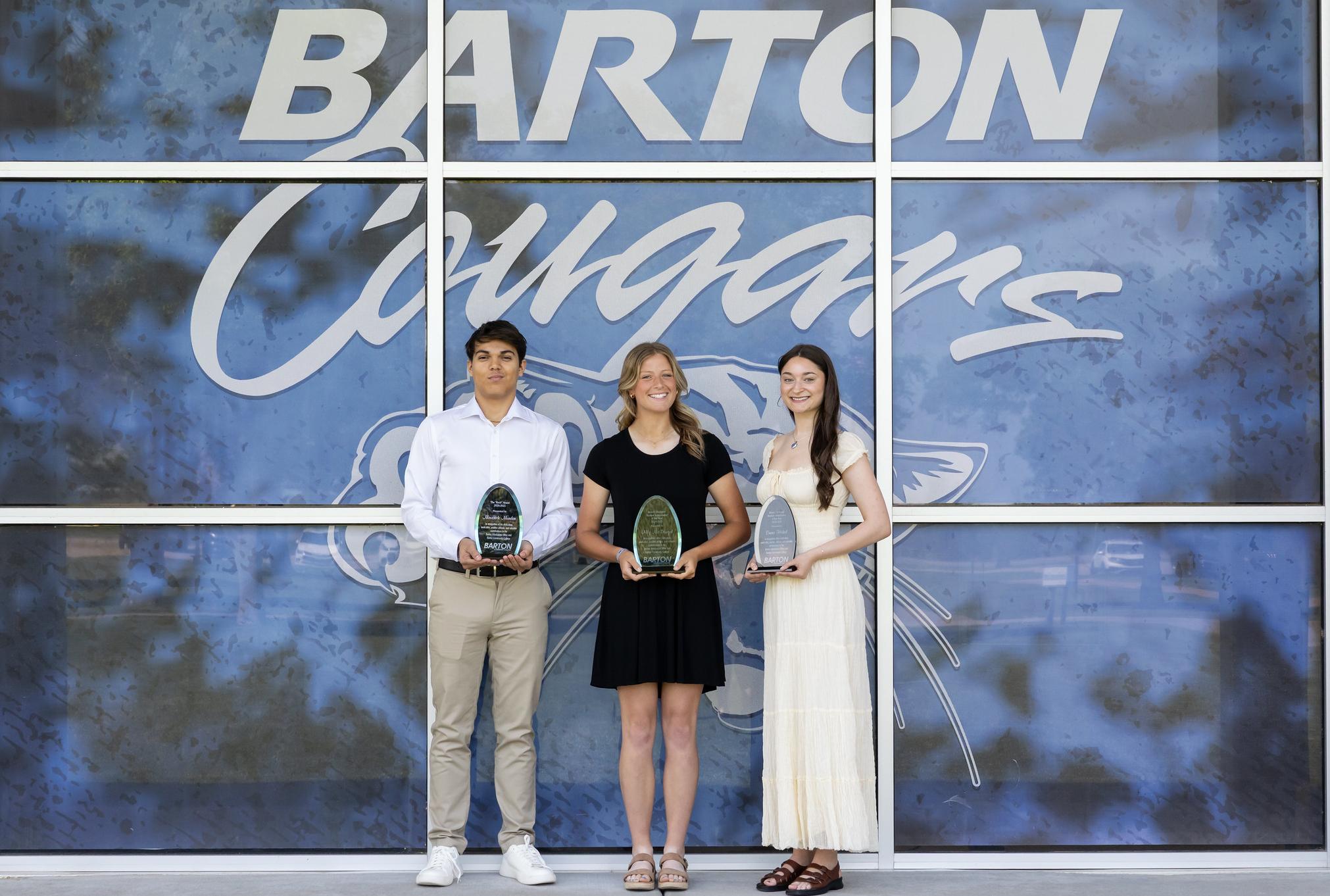 three students in front of a blue graphic window with a cougar mascot on the window