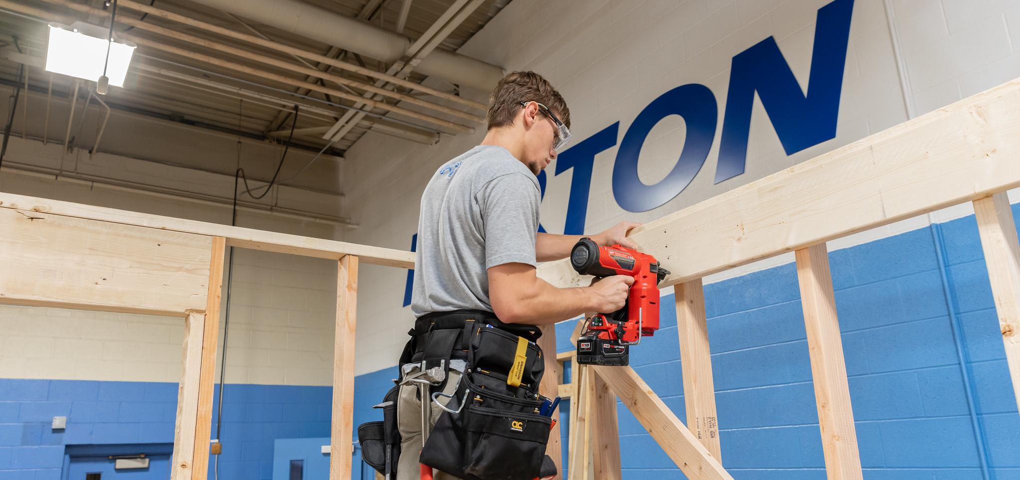 Student uses nail gun on framing in construction technology classroom