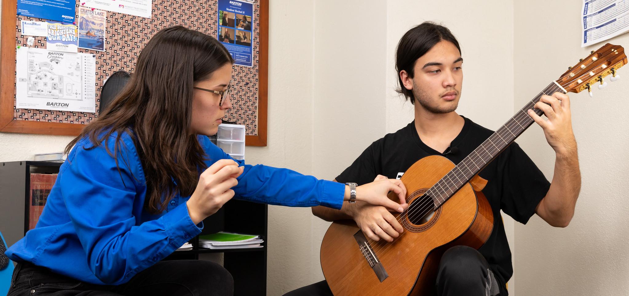 Music instructor helps student with guitar hand placement