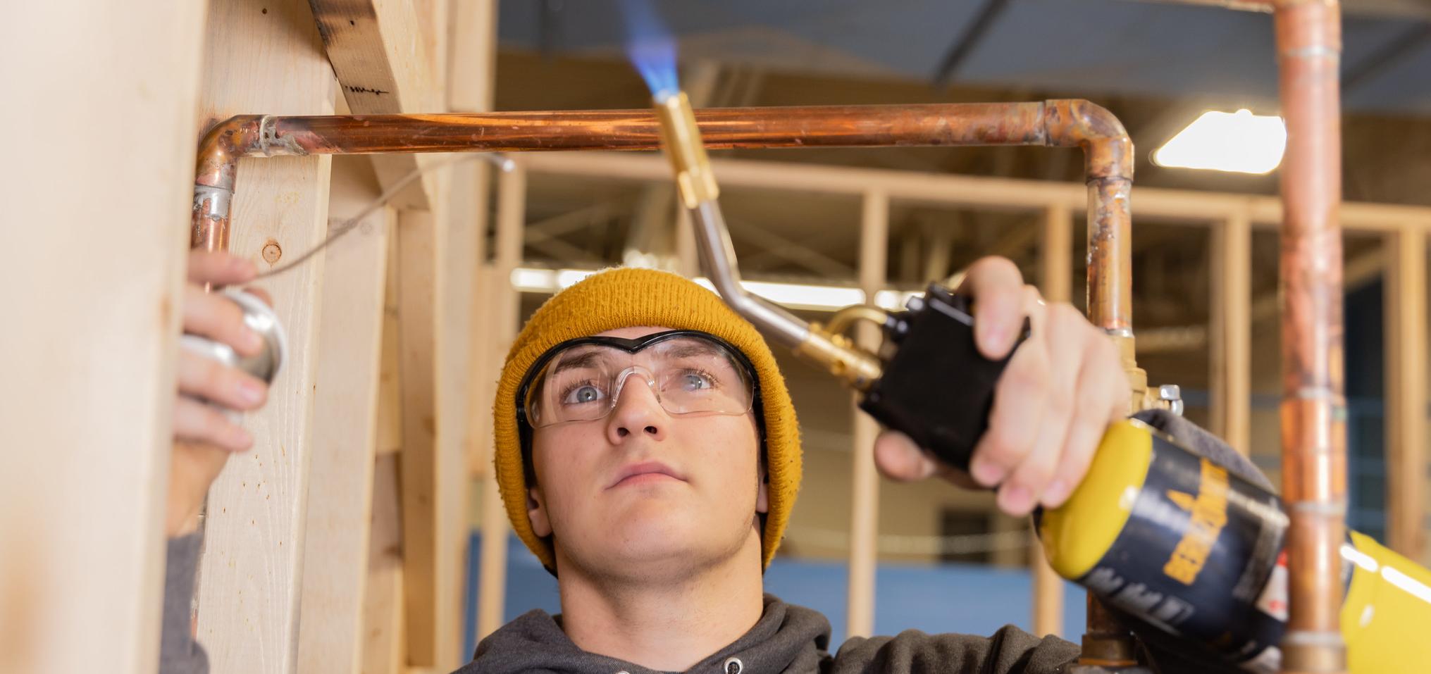 A plumbing student works on copper piping with a heat torch